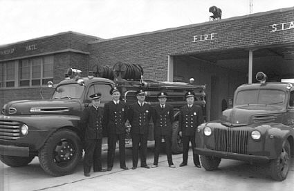 Black and White Photo from 1950 of 5 Firefighters and 2 Fire Engines
