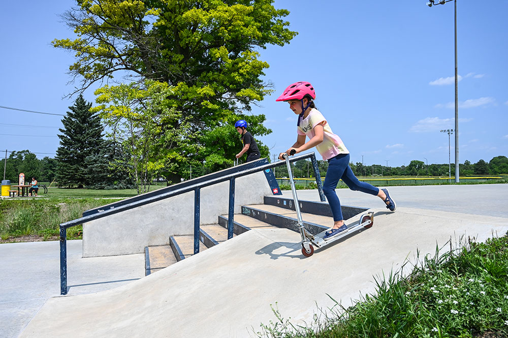 girl riding scooter down ramp at the skate park